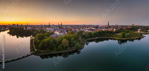 Panoramic aerial view capturing the Kobenhavn city skyline and park islands beautifully reflecting in tranquil lake waters during sunset light in Copenhagen, Denmark.