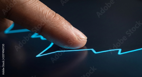 Close up of male finger touching glowing blue digital line graph on dark touch screen interface.