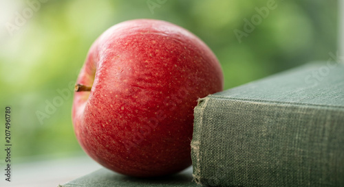 Fresh red apple resting on green hardcover book by the window, back to school and education concept.