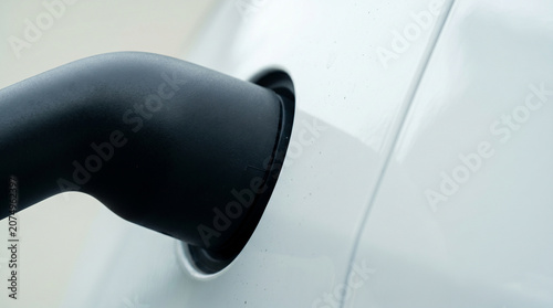 Close up of electric vehicle charging station cable plugged into modern white EV car.
