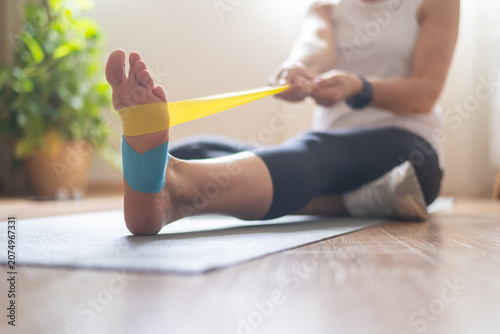 Foto Woman rehabilitating a foot injury with an exercise band and kinesiology tape du