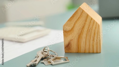 Slow pan across a desk showing a calculator, house keys, and a wooden house model. Real estate investment, mortgage planning, and home buying concept