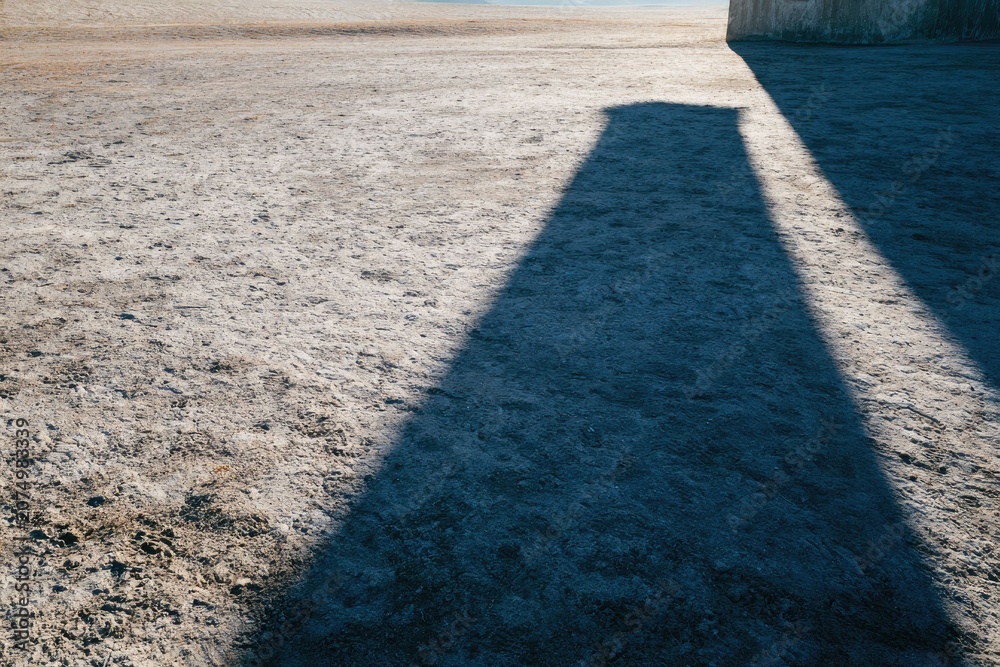 Obraz premium Long Shadow Cast by Large Wall on Flat Ground in Bright Outdoor Setting