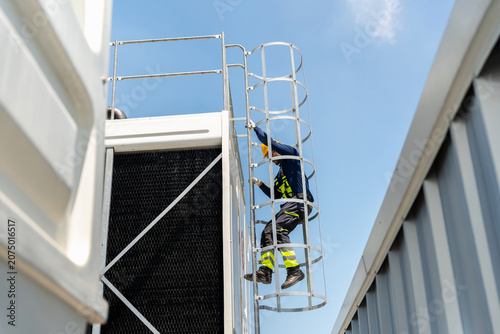 Technician man climbing a safety ladder to inspect industrial cooling system, Professional worker accessing HVAC equipment, Industrial maintenance worker in safety gear climbing a caged ladder