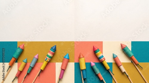 A creative and dynamic flat-lay composition featuring traditional wooden-fused rocket fireworks arranged to form a circle or circular frame. Each rocket features a decorative paper tube with various p