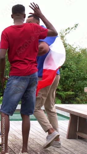 Vertical video: Grabbing flag, man in blue tee and khakis twirling on deck, celebrating with grill