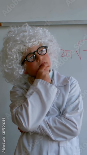 Vertical video: Posing boy in lab coat wig as scientist, tilting head touching chin at school board