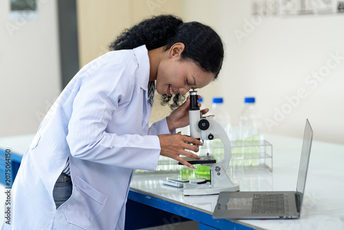 African American female scientist working with microscope and notebook computer in laboratory