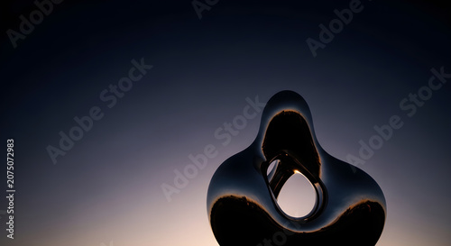 Abstract modern sculpture with a reflective surface against a gradient sky at dusk, artistic design