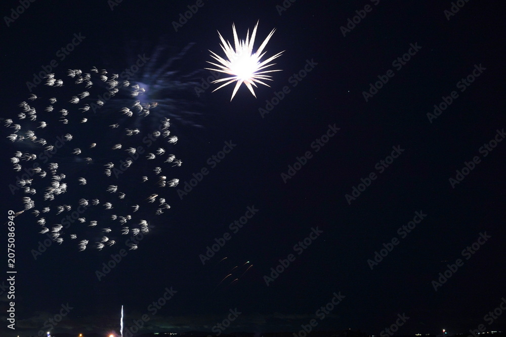 Fototapeta premium 夜空に広がる花火の爆発と星の軌跡。都市の灯りが遠くに点在する夜景。