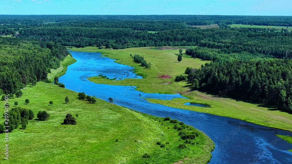 Obraz premium Meandering river flowing through vibrant green fields under a bright blue sky landscape