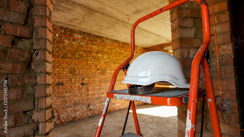 Konstfotografi Construction site safety helmet resting on an orange stepladder indoors