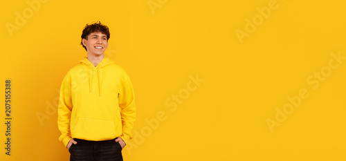 Canvastavla Smiling young man in yellow hoodie looking aside at copy space on yellow studio
