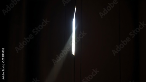 Ancient wooden door with keyhole illuminated by a diagonal beam of light, dramatic contrast.