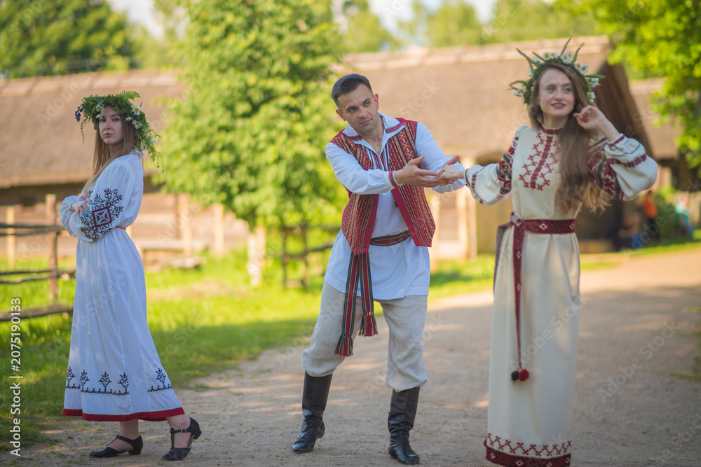Obraz premium Slavic youth dancing and flirting in traditional embroidered clothes inside historical village with copy space