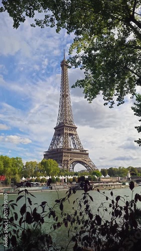 A scenic view of the Eiffel Tower framed by green tree leaves under a cloudy sky in the French capital
