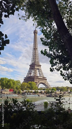 A scenic view of the Eiffel Tower framed by green tree leaves under a cloudy sky in the French capital