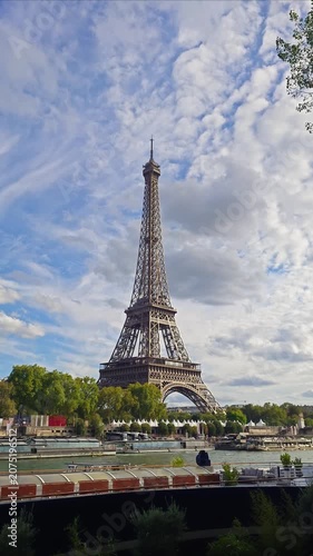 Eiffel Tower viewed from Seine riverbank on a cloudy day, with boats and trees in Paris