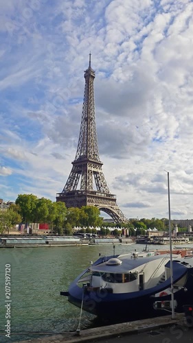 Eiffel Tower viewed from Seine riverbank on a cloudy day, with boats and trees in Paris