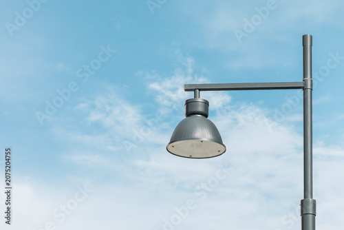 Modern metal street lamp on a pole against a blue sky with soft clouds and copy space