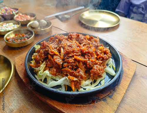 plate of spicy Korean stir-fried meat served on a hot sizzling plate with fresh cabbage and onions, topped with sesame seeds.showcasing authentic Korean cuisine.