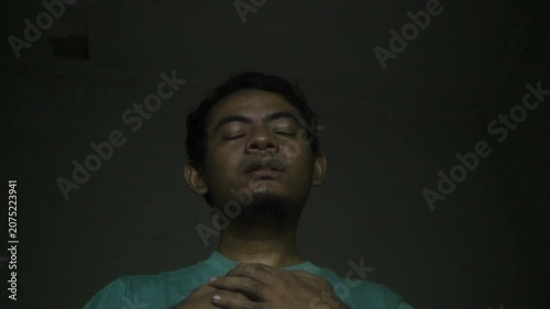 Asian Man Experiencing Chest Pain And Anxiety Symptoms In Dimly Lit Room With Dark Background