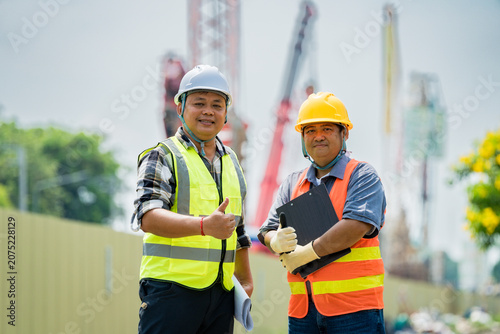 Asian engineers posing at a construction site. Professionals in safety gear show confidence in urban development and project management, highlighting teamwork and success.