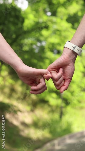 Two girls holding hands. Close-up of two female hands, on a blurred green background of the park. Symbol of trust, tenderness and LGBT relationships. Love concept. Two women holding hands