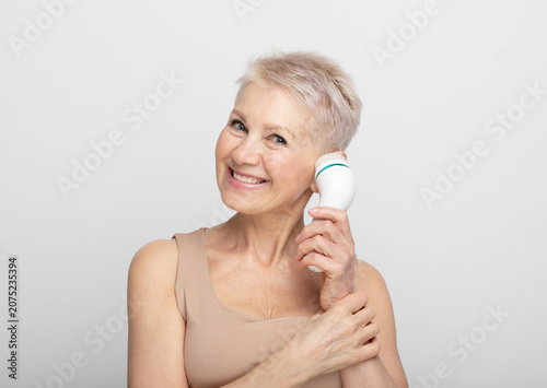 Beautiful 60s woman holding a massager in her hand. Spa technique skincare ads.