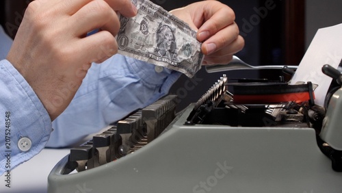 Foto Hands hold up a crumpled one dollar banknote over a vintage typewriter with pape