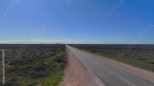 Aerial drone shot flying over the Nullarbor Plain sign at close range and moving forward along the endless straight road through the barren outback