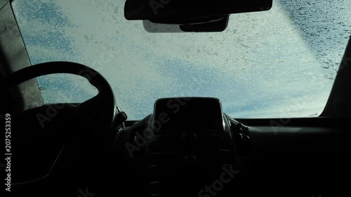 View from inside the car, a man applying foam to the windshield. Car wash outside. Cleaning the car