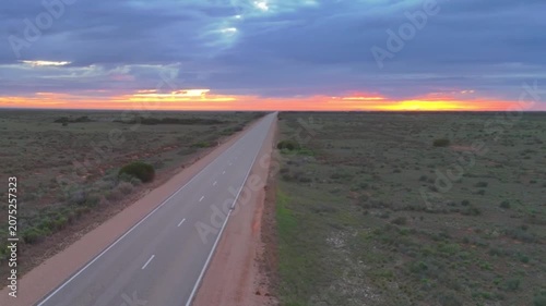 Aerial drone shot panning across the barren Nullarbor Plain with an endless straight road and a red sunrise on the horizon