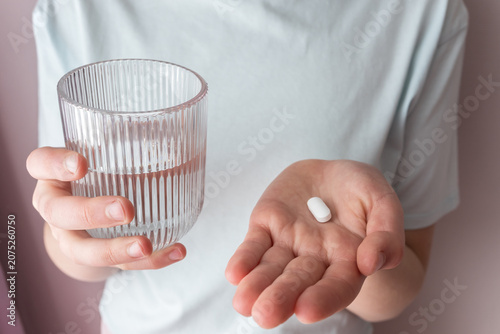 Girl is ill and stay at home. Woman holding pill and glass with water in the hands.