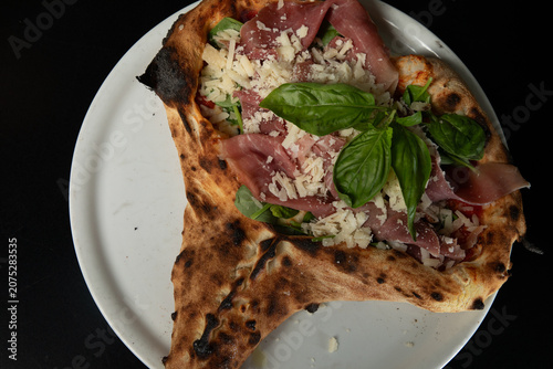 Schilderij op canvas Pizza avec une garniture de jambon et basilic sur une assiette blanche