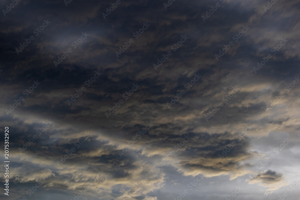 Fototapeta premium Dark turbulent cloudscape with golden-tinged wave-like formations swirling across a brooding sky