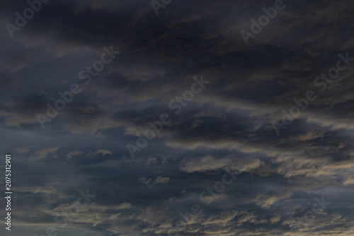 Photos Dark brooding layered storm clouds with warm golden edges against deep blue-grey