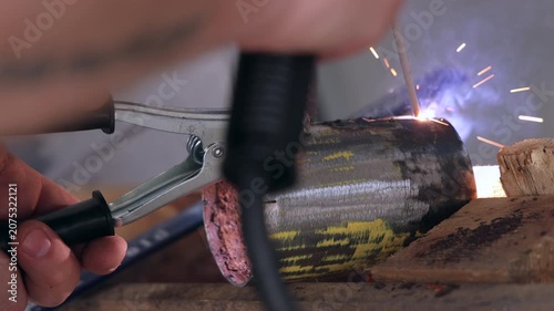 Close up of a welding ground clamp attached to a metal pipe on a workbench