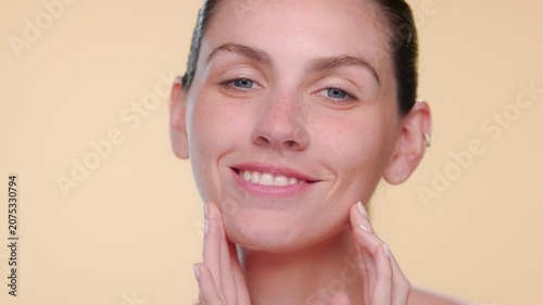 Closeup of fair-skinned freckled Latin woman strokes her forehead showcasing skin smoothness on beige bg | Skin care commercial concept