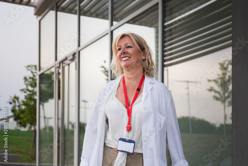 Foto Senior female physician wearing a lab coat and id badge, smiling while walking o