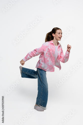 Happy teenage girl running with a cheerful smile. Studio portrait expressing energy, movement, freedom, playfulness and active lifestyle.