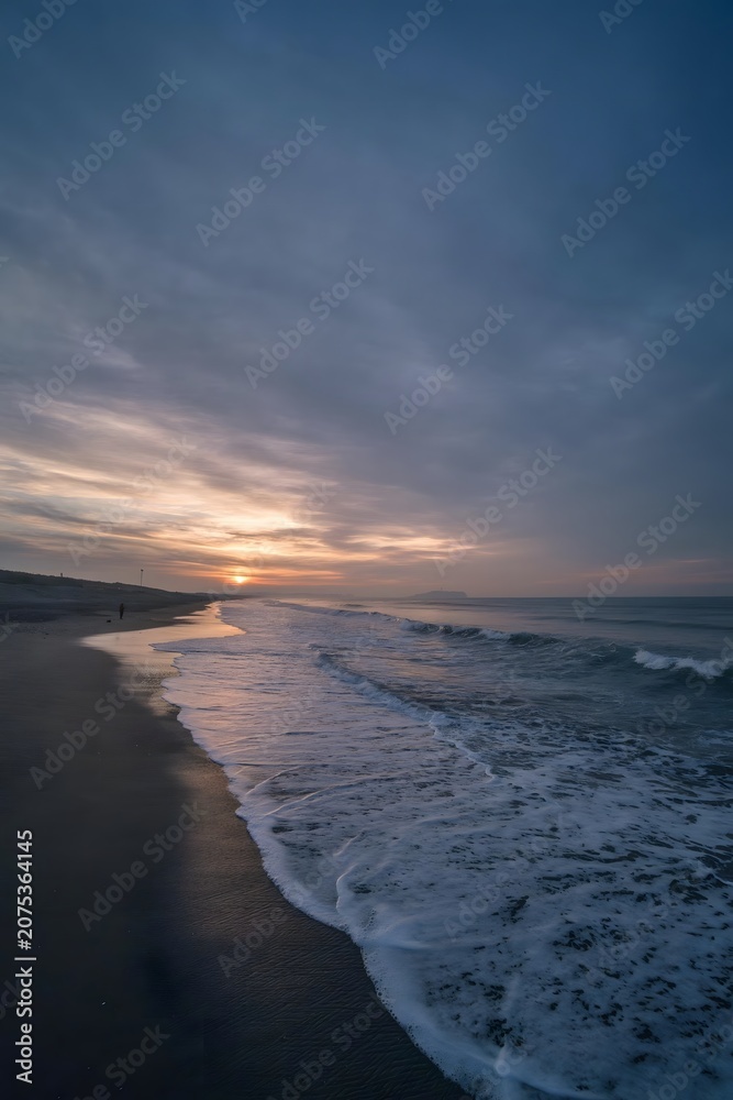Fototapeta premium Sunset waves along a quiet sandy beach under a dramatic cloudy sky