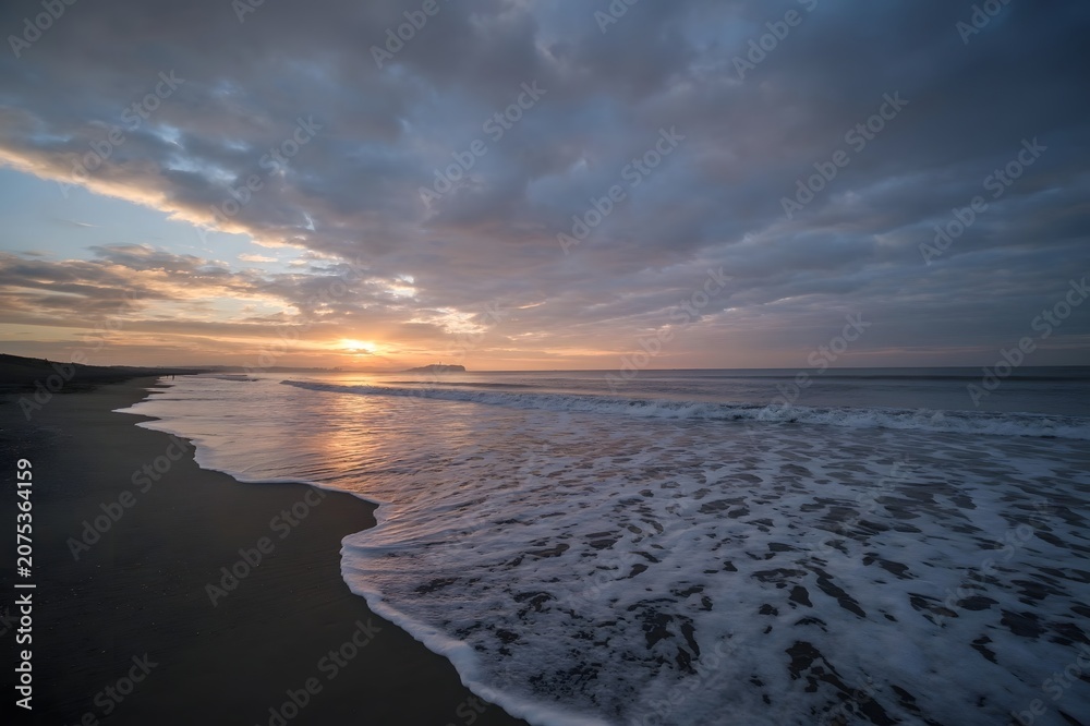 Obraz premium Dramatic Sunset on a Quiet Sandy Beach with Rolling Waves