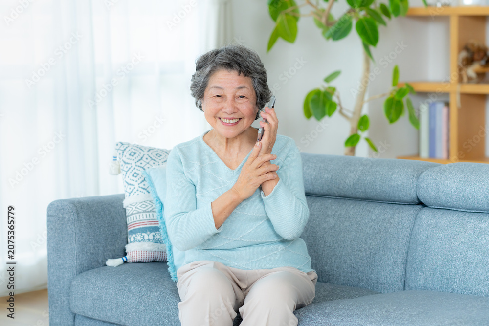 Naklejka premium リビングで電話するシニア女性