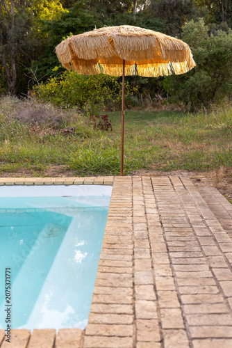 Straw parasol providing shade by swimming pool in garden