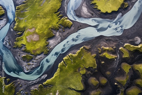 Aerial view of winding river channels cutting through dark sediment and green mossy terrain, forming abstract natural patterns