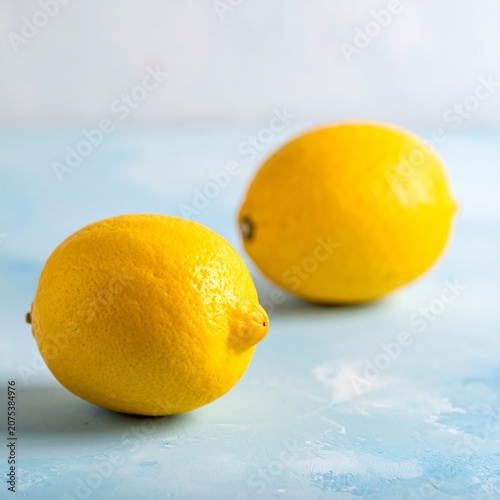 A close-up of two vibrant yellow lemons on a light blue surface