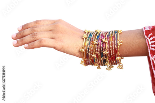 Elegant woman wearing colorful traditional indian bangles with small golden bells on her wrist captured in a close up shot against a plain white studio background.