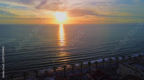 A breathtaking panoramic view of a dramatic golden sunset over the Mediterranean Sea in Agropoli, Cilento coast. The sky is filled with vibrant hues of orange, pink, yellow, and blue clouds, while the