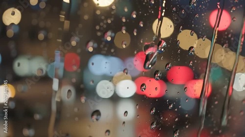 Raindrops Dripping Down a Dark Car Window with Blurry Colorful City Traffic Lights